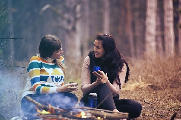 two friends talking by campfire smiling